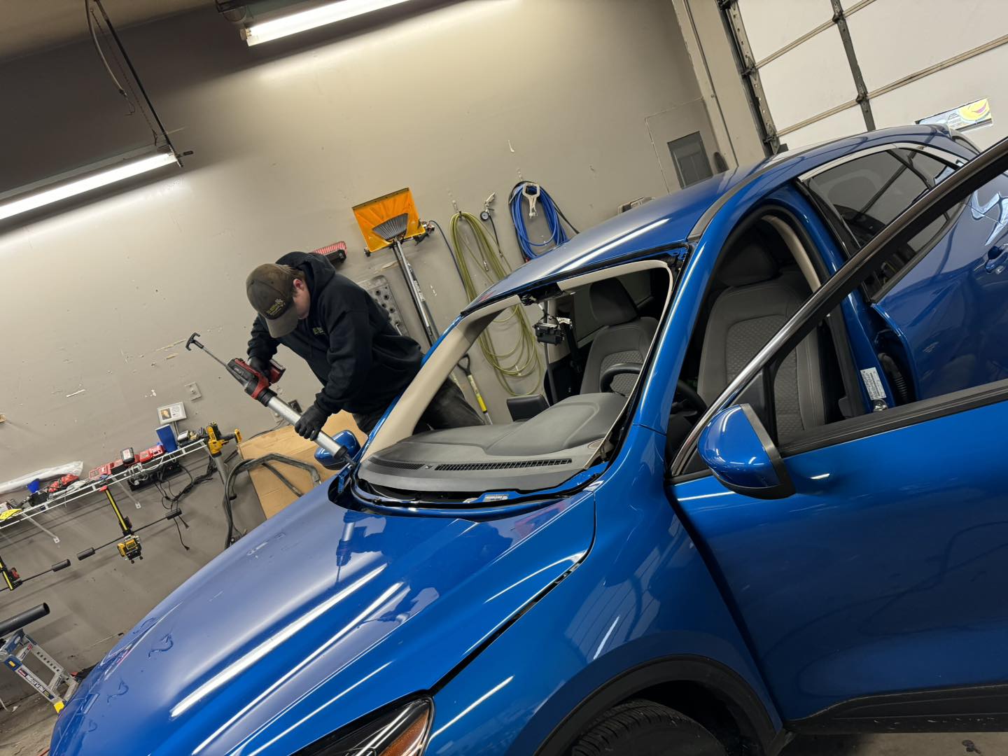 Technician applying urethane sealant during windshield replacement on a blue SUV